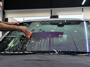 Installer using an orange squeegee to remove water beneath windshield protection film.